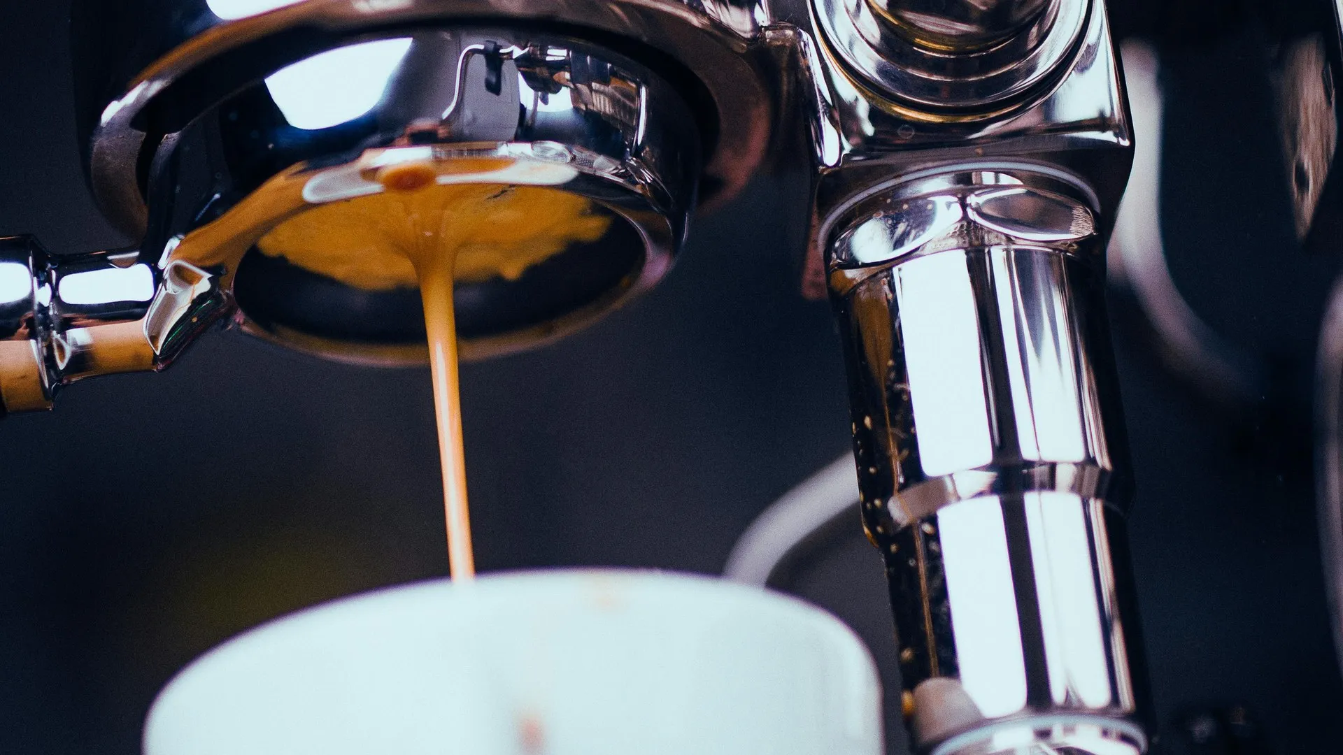 Espresso extracting from a naked portafilter into a white cup, golden crema visible