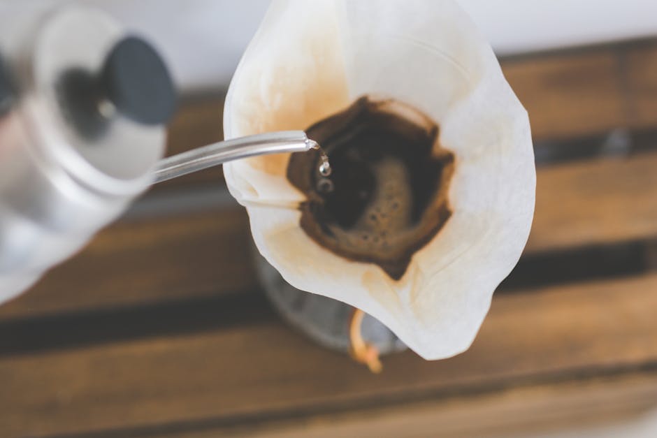 Close-up of pour over coffee brewing, with hot water being poured from a gooseneck kettle through a paper filter in a Chemex