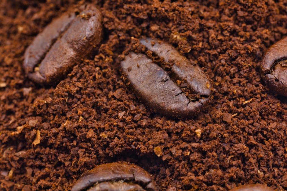 Roasted coffee beans resting in a bed of fine ground coffee, illustrating the contrast between whole beans and the grounds they produce
