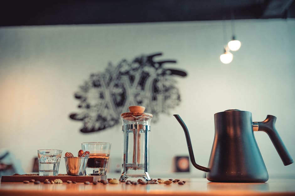 An elegant coffee setup featuring a French press, pour kettle, glasses, and scattered coffee beans