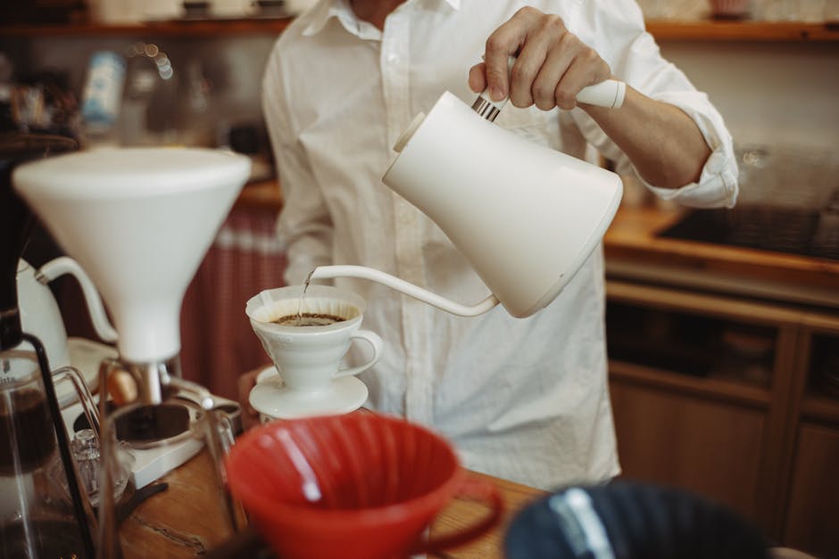 Barista pouring hot water from a gooseneck kettle over a coffee dripper, demonstrating precise temperature control