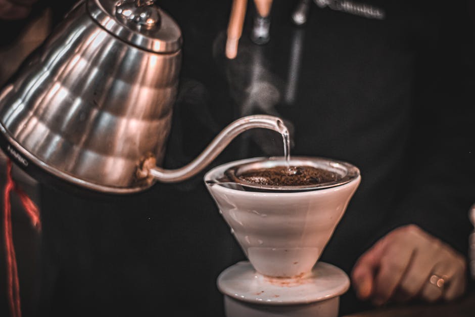 Hot water being poured in a controlled spiral over coffee grounds in a pour-over dripper, with steam rising