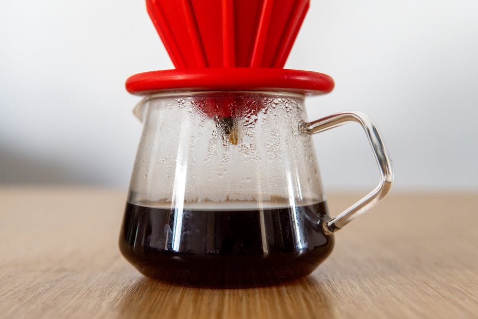 Steam rising from a glass V60 dripper as freshly brewed coffee drips into a carafe below